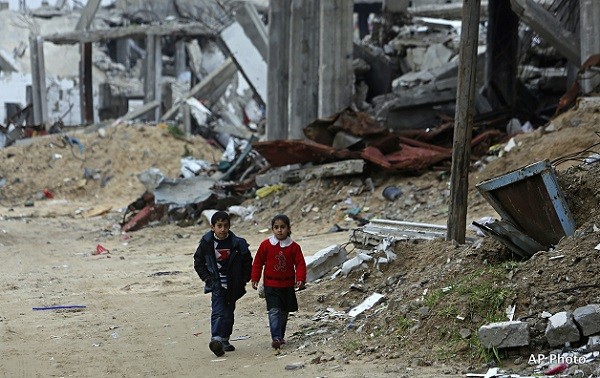 A Palestinian brother and sister walk in front of a building which was destroyed in last summer's Israel-Hamas war, in the Shijaiyah neighborhood of Gaza City, northern Gaza Strip, Monday, Feb. 23, 2015. (AP Photo/Adel Hana)
