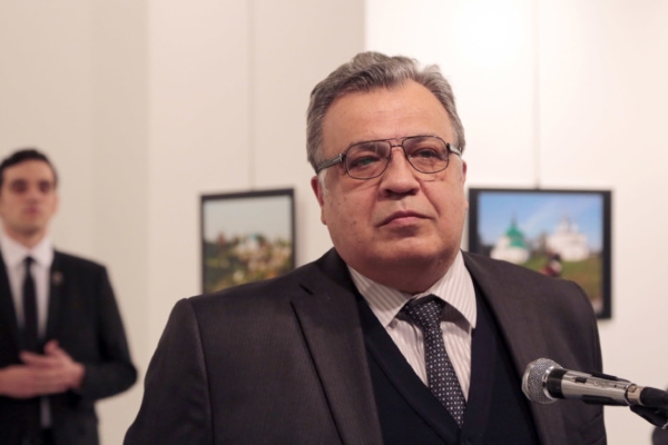 The Russian Ambassador to Turkey Andrei Karlov speaks a gallery in Ankara Monday Dec. 19, 2016. A gunman opened fire on Russia's ambassador to Turkey Karlov at a photo exhibition on Monday. The Russian foreign ministry spokeswoman said he was hospitalized with a gunshot wound. The gunman is seen at rear on the left. (AP Photo/Burhan Ozbilici)
